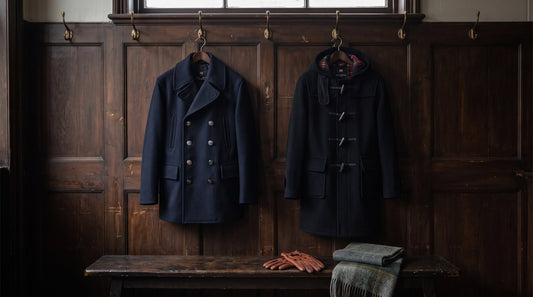 Navy reefer jacket and black duffle coat on brass hooks against a dark panelled wall