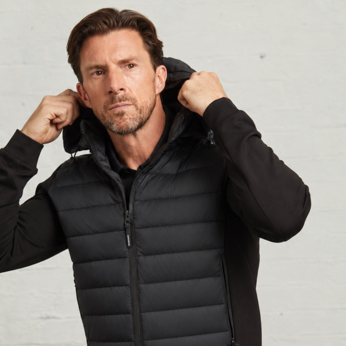 Bale jacket in Black on a model holding the quilted hood, knitted sleeves visible