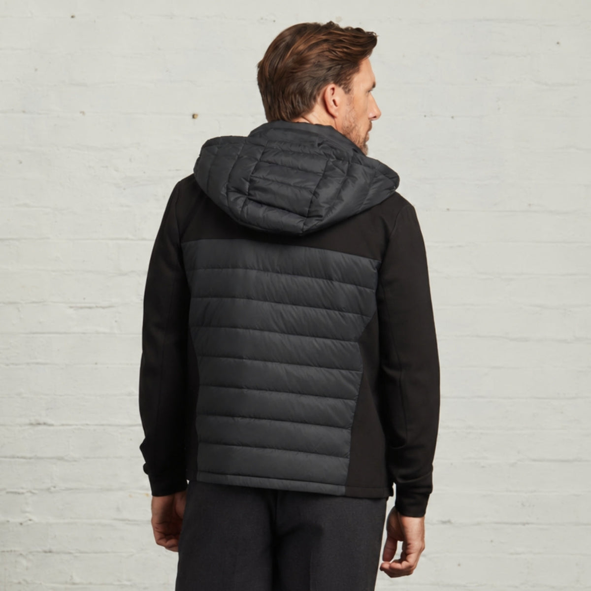 Back view of the Bale hybrid jacket in Black showing the quilted hood and knitted side panels