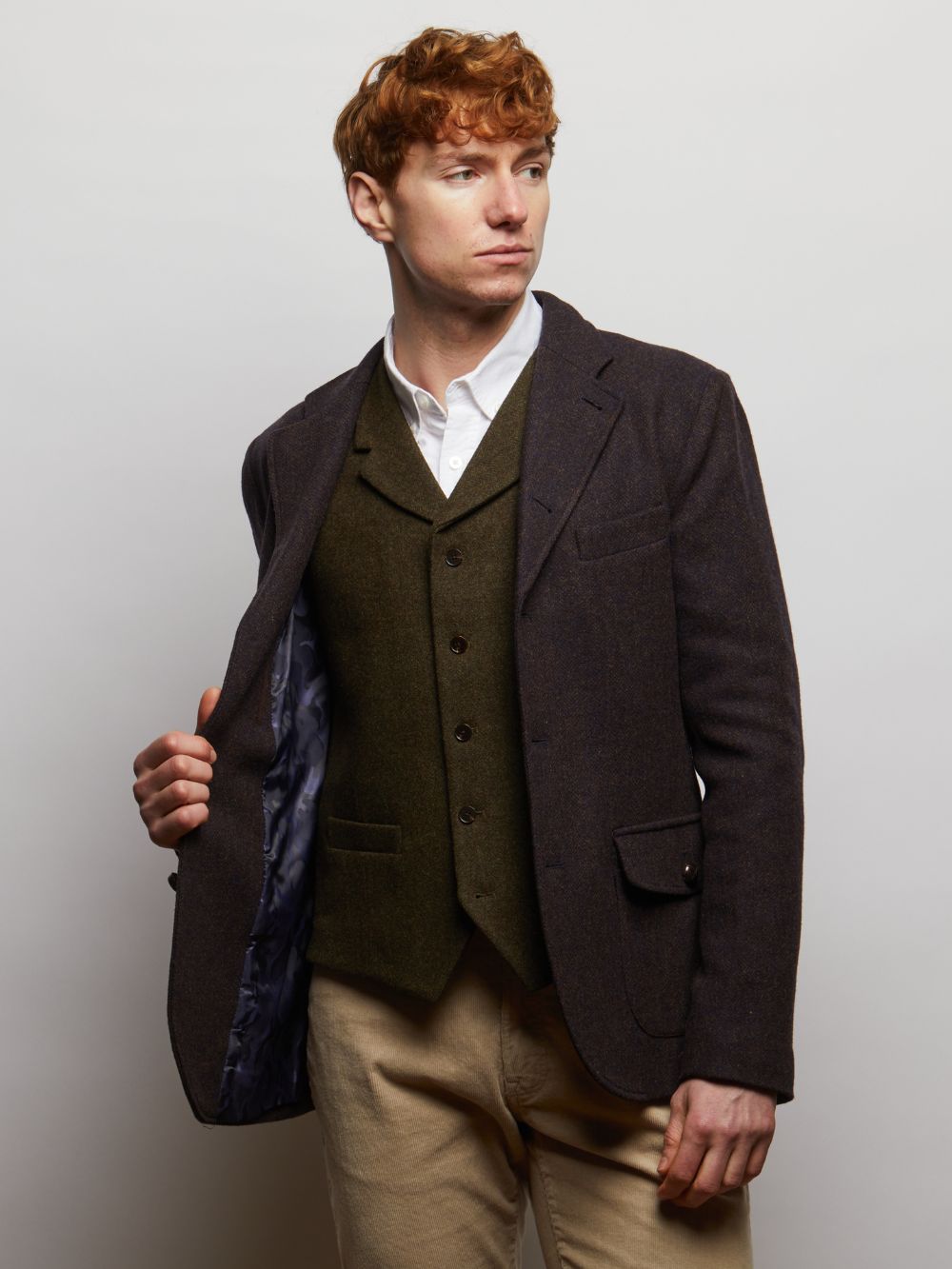 Allenby tweed blazer in a dark colourway worn open over a green tweed waistcoat on a model