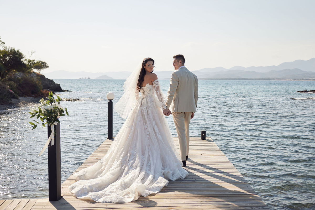 Couple in wedding attire standing on a dock by the water
