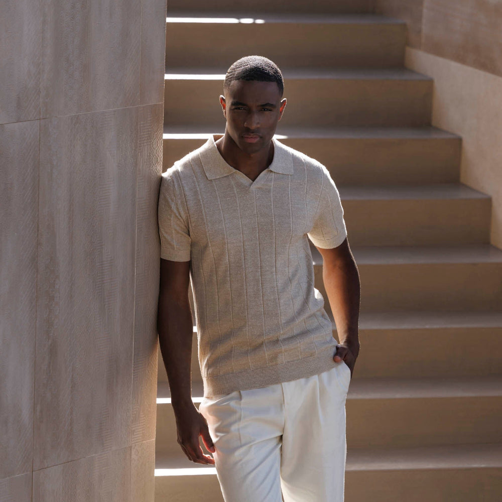 Man standing on a set of stone steps wearing a light-colored polo shirt and white pants.