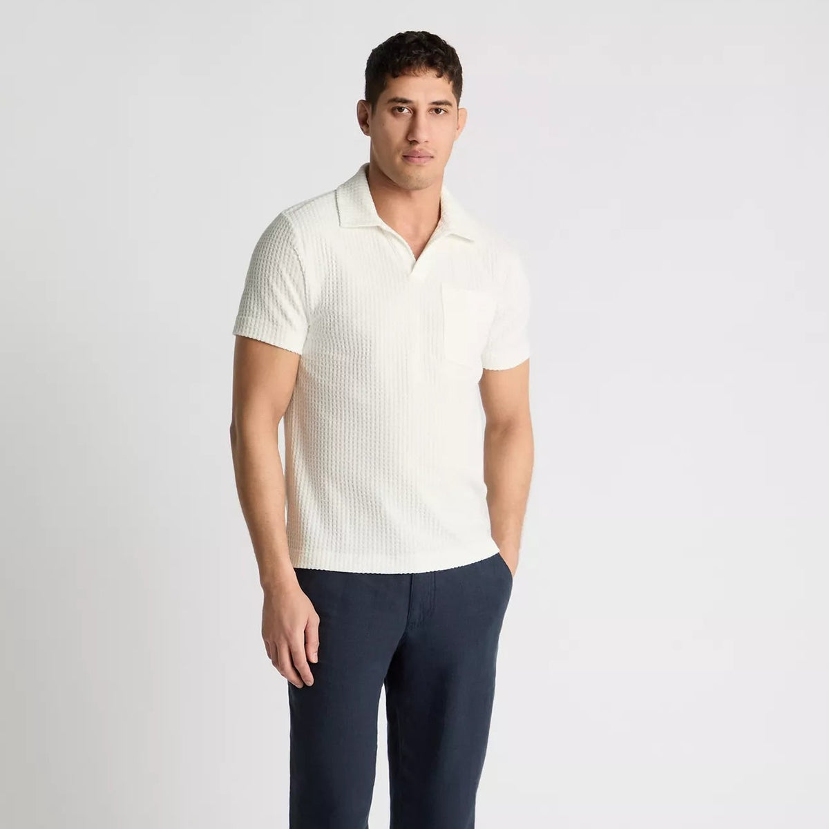 Man wearing a white polo shirt and navy pants on a light gray background