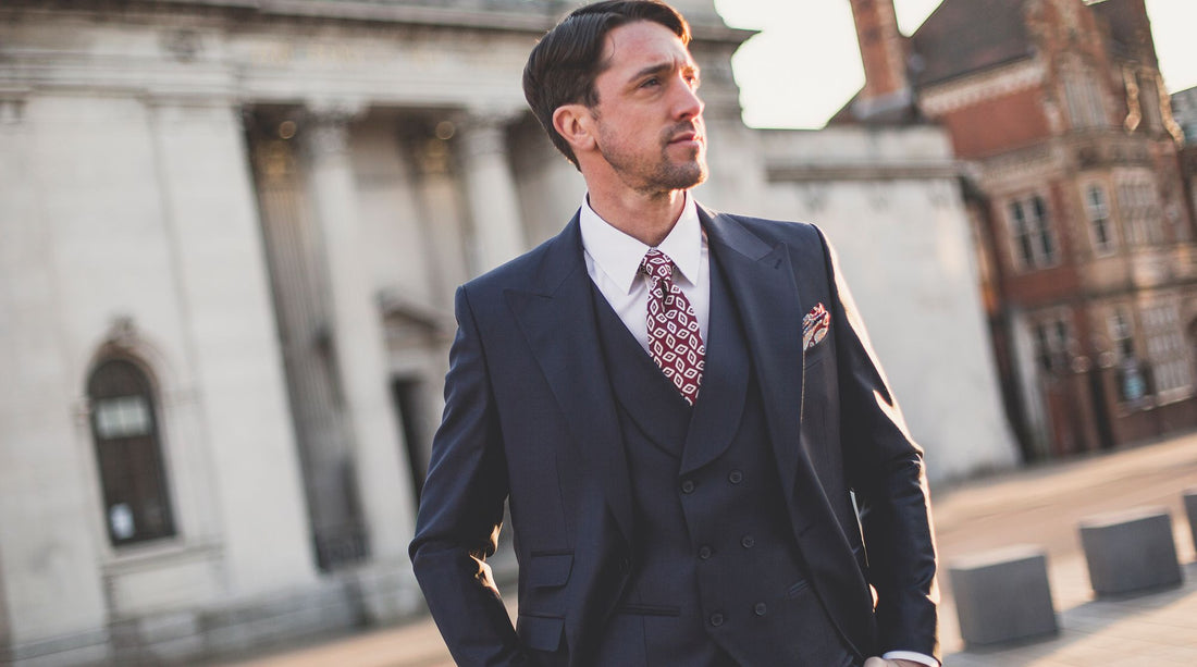 Man in a navy three-piece suit and burgundy tie in a city square